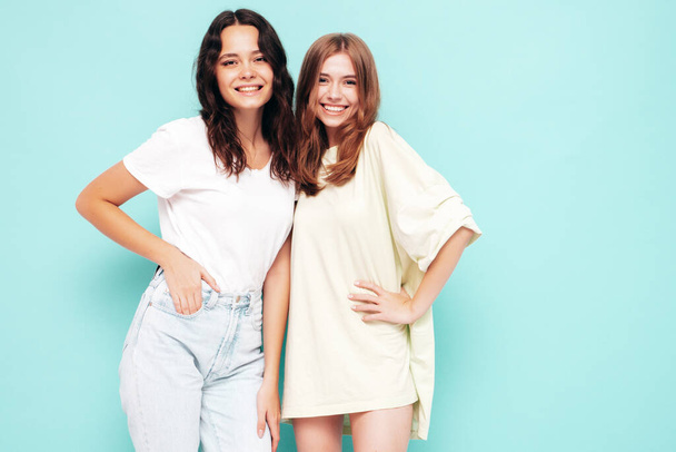 Two young beautiful smiling brunette hipster female in trendy summer clothes. Sexy carefree women posing near blue wall. Positive models having fun. Cheerful and happy  - 写真・画像