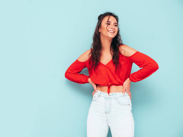 Young beautiful smiling female in trendy summer red top and jeans clothes. Sexy carefree woman posing near blue wall in studio. Positive brunette model having fun. Cheerful and happy - Foto, afbeelding