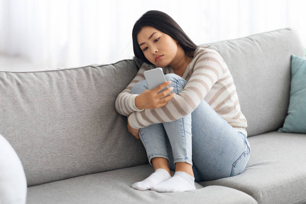 Upset Young Asian Woman Looking At Smartphone Screen While Sitting On Couch - Foto, imagen