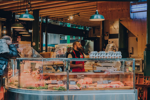 London, UK - October 17, 2021: Man working at the fresh meat and poultry stand in Borough Market, one of the largest and oldest food markets in London. - 写真・画像