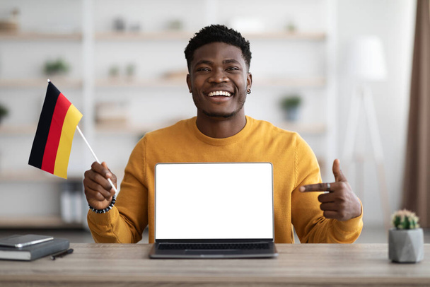 Excited black guy student showing flag of Germany and laptop - Foto, imagen