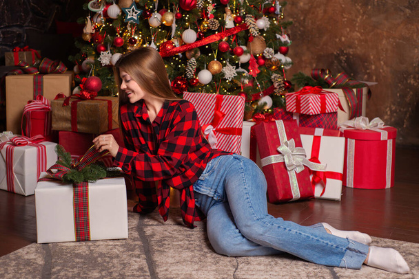 Young beautiful woman near a christmas tree with gifts in a luxurious interior - Foto, Imagen