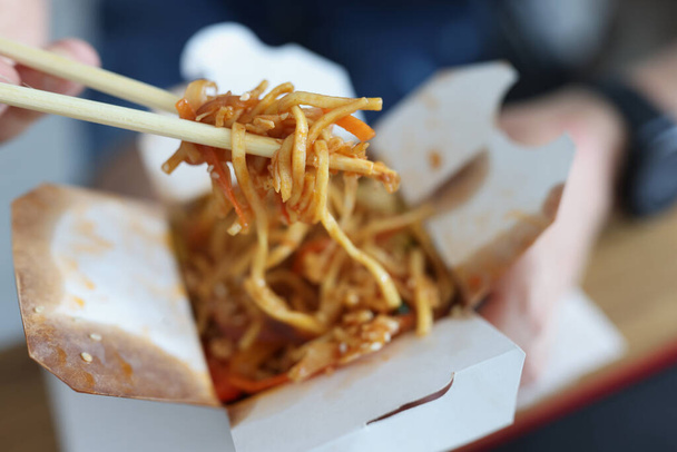 Man eating chinese noodles with chopsticks out of paper box closeup - Foto, Imagen