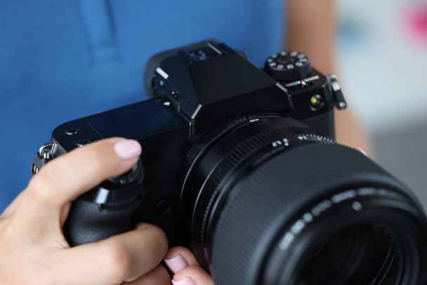 Женщина держит в руках профессиональную черную камеру и выпрямляет объектив крупным планом - Фото, изображение