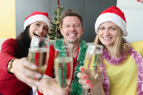 Hombre y mujeres en sombreros de santa bebiendo champán cerca del árbol de Navidad - Foto, Imagen