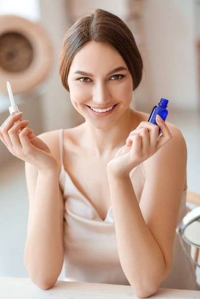 Young smiling woman with bottle of essential oil sitting at table in room - Foto, imagen