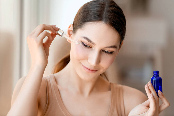 Beautiful woman applying natural essential oil on face - 写真・画像