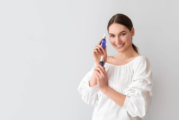 Smiling woman holding bottles of essential oil on light background - Photo, Image