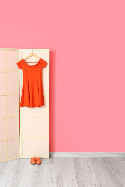 Pantalla plegable ligera con vestido rojo y zapatos cerca de la pared rosa - Foto, imagen