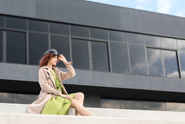 Młoda kobieta w skórzanej czapce w pobliżu nowoczesnego budynku na zewnątrz - Zdjęcie, obraz