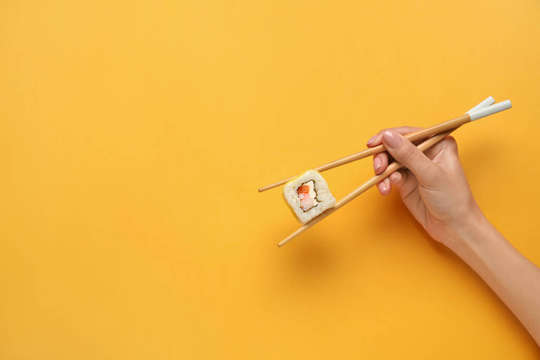 Frau hält Essstäbchen mit köstlichen Sushi-Rollen auf farbigem Hintergrund - Foto, Bild