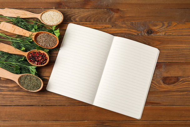 Открытая книга рецептов и ложки с различными специями на деревянном фоне - Фото, изображение