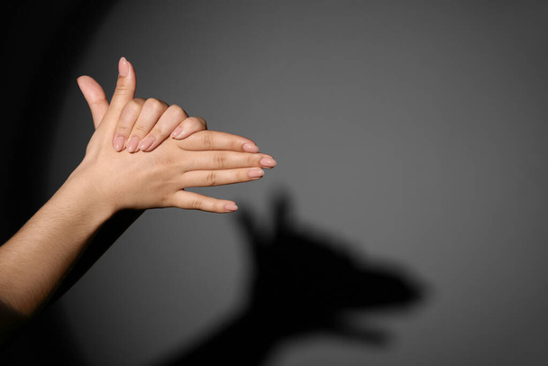 Frau macht Schattenhund mit ihren Händen auf dunklem Hintergrund - Foto, Bild