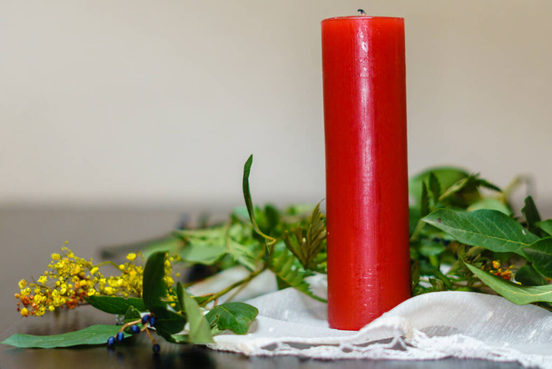 Рождественские украшения: красная свеча, зеленые листья, ягоды на белой скатерти - Фото, изображение