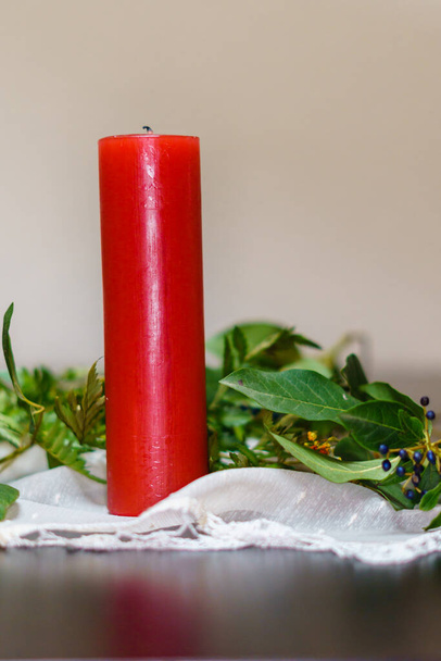 Decorazioni natalizie: candela rossa, foglie verdi, bacche su una tovaglia bianca - Foto, immagini