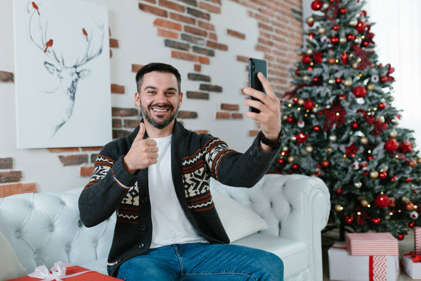 男自身は自宅でクリスマスを祝います,携帯電話上のアプリケーションを使用してビデオで通信する友人からの挨拶を受けます - 写真・画像