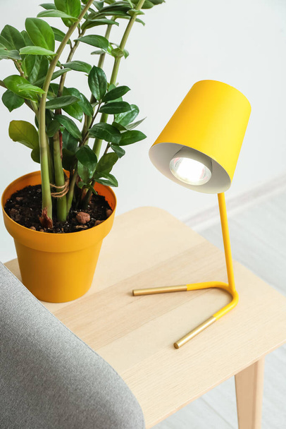 Table with yellow lamp and houseplant near light wall - Photo, Image