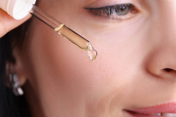 Woman holding dropper with cosmetic oil near her face closeup - Fotoğraf, Görsel