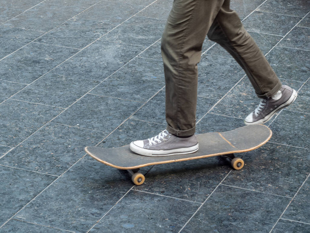 The teenager goes for a drive on a skateboard. The left foot is on the skateboard and the right foot is pushing off. Close-up. - Photo, image