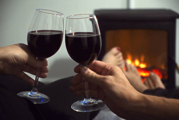 Couple sitting in a cozy room with fire place on a sofa with glass of wine - Foto, afbeelding