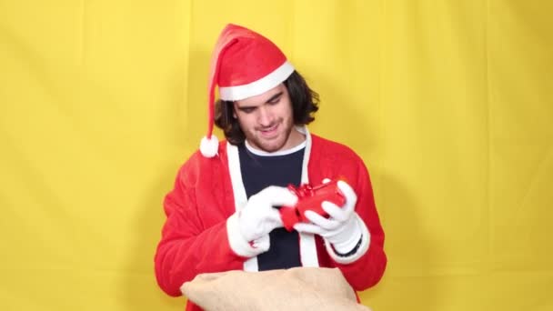 El hombre sonriente vestido como Santa Claus muestra los regalos tomados de un gran saco de yute. Concepto de alegría y felicidad para una hermosa Navidad! - Metraje, vídeo