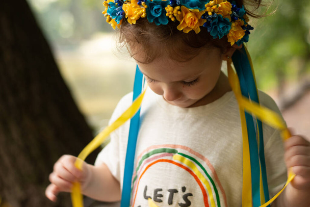 Menina triste com decoração popular ucraniana em sua cabeça. Criança tocando fitas de grinalda enquanto estava ao ar livre - Foto, Imagem