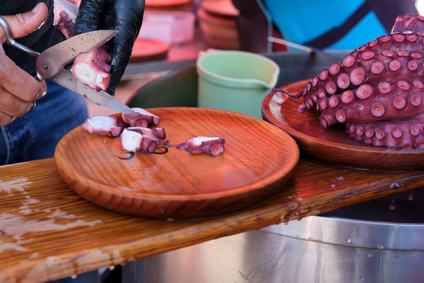 Неузнаваемый человек режет осьминога в галисийском стиле и кладет его на деревянные тарелки. - Фото, изображение