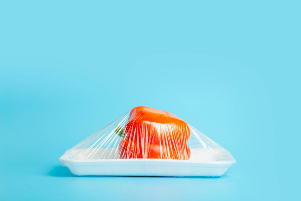 Vegetables in plastic packaging from the supermarket are minimal. Pepper in cellophane and non-degradable plastic on a blue background. Biodegradable product packaging, environmental protection - Foto, Bild