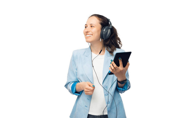 Молодая женщина в светло-голубой куртке держит планшет и слушает что-то в наушниках на белом фоне. - Фото, изображение