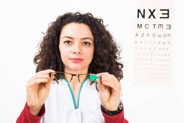Closeup of a serious woman doctor holding eyeglasses with eye chart behind - isolated on white.  - Foto, Bild