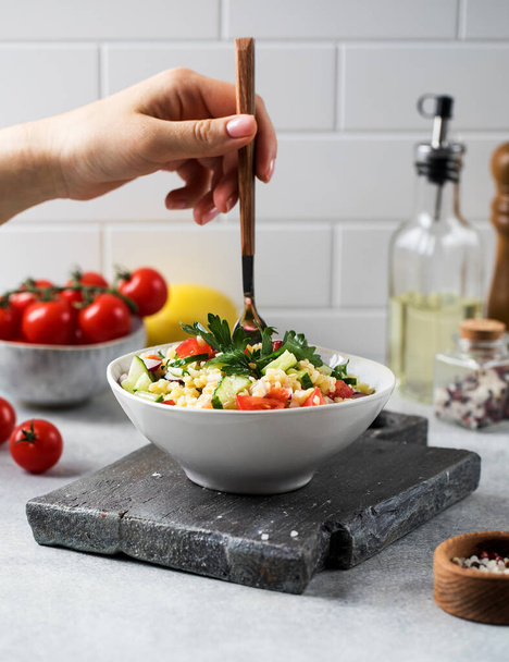  A hand holds a fork in a vegetarian salad of bulgur and vegetables. - 写真・画像