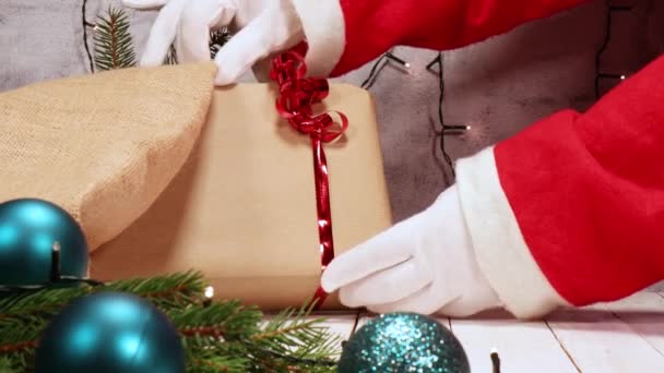 ¡Navidad! Santa Claus arregla los regalos bajo el árbol de Navidad. Decoraciones navideñas alrededor y luces en el fondo. - Metraje, vídeo