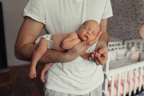 Cropped portrait of father holding sleeping newborn baby on his arm. Newborn girl sleeping like koala. Newborn baby in diaper in fathers hands. Selective focus. Film grain - Photo, image