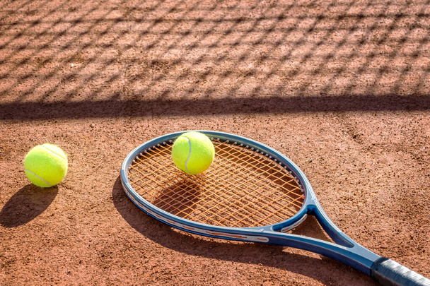 Теннисная ракетка и новый теннисный мяч на корте из красной глины. - Фото, изображение