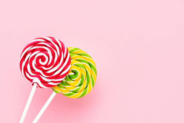 Two colorful lollipops on a white stick on a light pink background. Top view, copy space - Φωτογραφία, εικόνα