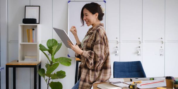 Podekscytowana azjatycka kobieta siedzi na swoim stanowisku pracy, zachwycona otrzymaniem oferty pracy po wywiadzie mailowym na laptopie. - Zdjęcie, obraz