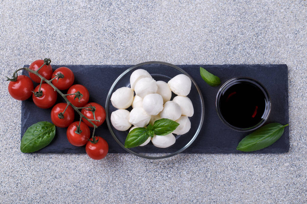 Mozzarella-Käse, Basilikum und Tomatenkirsche auf grauem Steintisch. Zutaten für italienischen Caprese-Salat - Foto, Bild