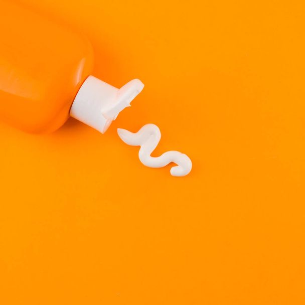 Белый крем от загара выходит из оранжевой бутылки на оранжевом фоне. Высокое качество фото - Фото, изображение