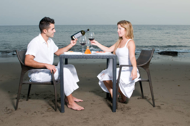 Young couple dressed in white celebrating a romantic dinner on the beach - Photo, Image