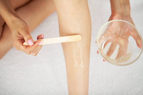 Vrouw tijdens de procedure van waxen vrouwen benen met wax strips op vrouwen benen thuis. - Foto, afbeelding