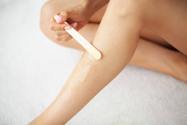 Mulher durante o procedimento de encerar as pernas das mulheres com tiras de cera nas pernas das mulheres em casa. - Foto, Imagem