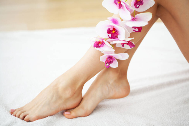 Las piernas largas de una mujer con una manicura fresca y flores de orquídea - Foto, Imagen