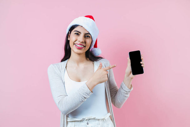 Portrait of young latin woman holding mobile phone with copy space in a christmas concept on pink background - Fotoğraf, Görsel
