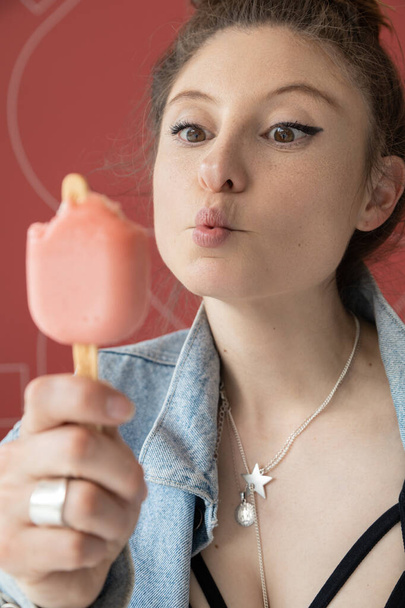 details of the face of a beautiful young woman having fun while eating ice cream, lifestyle and joy with food, wearing necklace and makeup in the daytime - Photo, Image