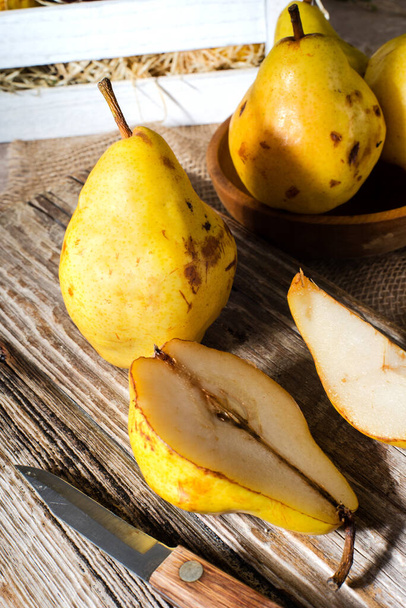 Sliced halves or slices of fresh sweet ripe yellow pears, next whole pears and cutting kitchen Board on brown wooden table background, close-up. - Fotografie, Obrázek