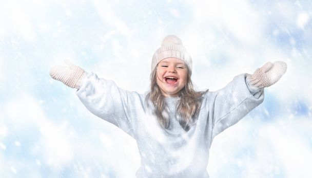 Glückliches Kindermädchen mit Hut und Handschuhen fängt Schnee beim Spaziergang - Foto, Bild