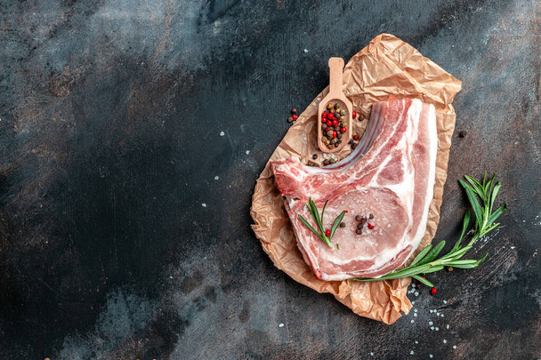 Raw meat with herbs and spices on dark background. Raw Pork meat chop steak. Restaurant menu, dieting, cookbook recipe. Top view. - Фото, изображение