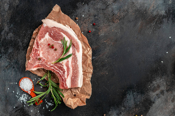 Raw meat with herbs and spices on dark background. Raw Pork meat chop steak. Restaurant menu, dieting, cookbook recipe. Top view. - Foto, Imagem