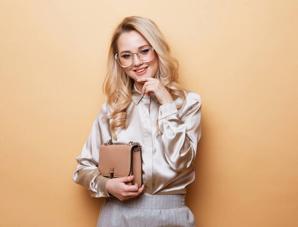 Lifestyle, fashion and people concept: Beautiful young blond woman holding handbag over beige background. - Fotografie, Obrázek