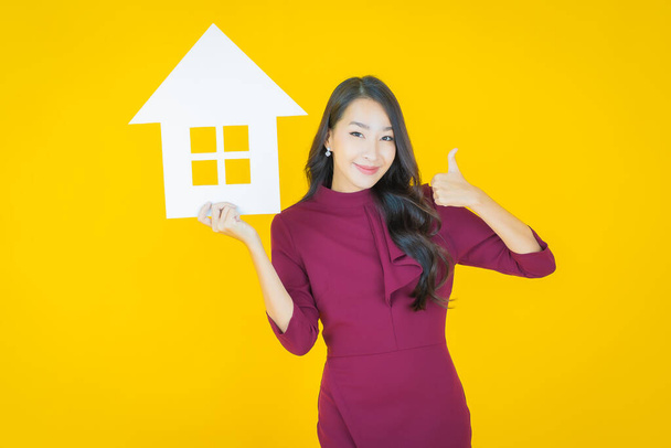 Portrét krásná mladá asijská žena s domem nebo domácí papír znamení na barevném pozadí - Fotografie, Obrázek